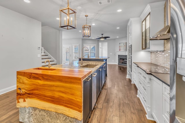 kitchen featuring pendant lighting, wood-type flooring, a center island with sink, white cabinets, and ceiling fan with notable chandelier