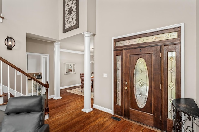 foyer with decorative columns, dark hardwood / wood-style flooring, a towering ceiling, and ornamental molding