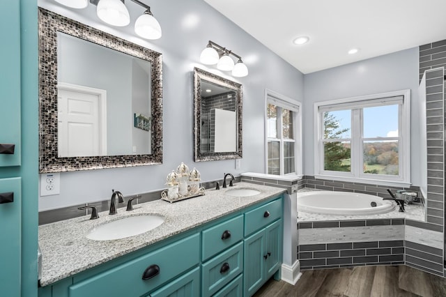 bathroom with wood-type flooring, vanity, and a relaxing tiled tub