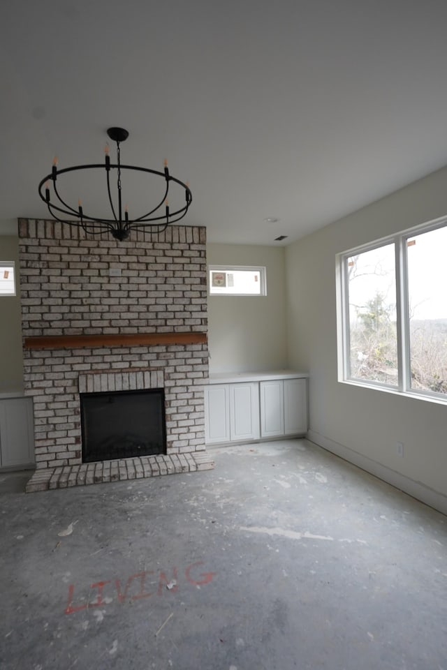 unfurnished living room with a notable chandelier, a brick fireplace, and concrete floors