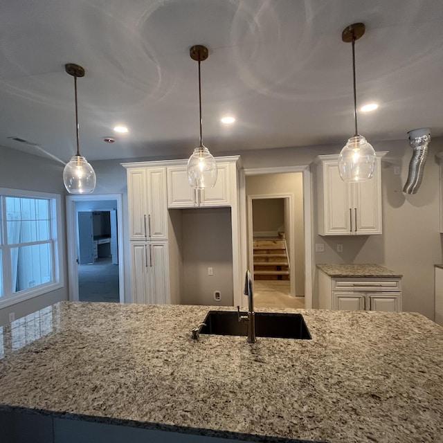 kitchen with white cabinetry, sink, pendant lighting, and light stone counters