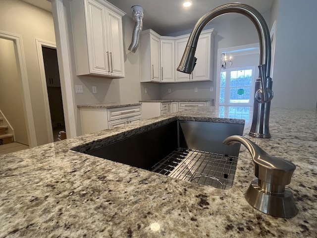 kitchen with white cabinets, light stone countertops, and sink