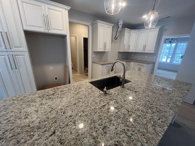 kitchen with light stone countertops, sink, pendant lighting, and white cabinets