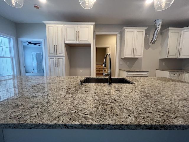 kitchen featuring light stone counters, sink, white cabinetry, and ceiling fan