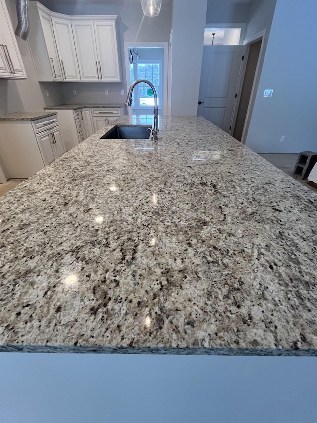 kitchen featuring light stone countertops, white cabinetry, and sink