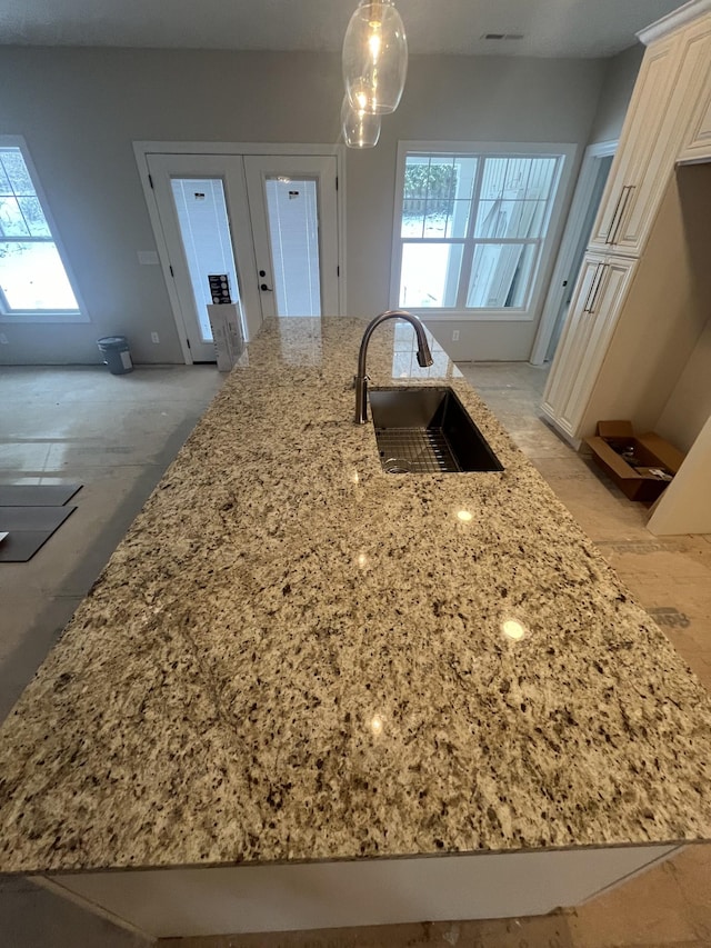 kitchen with light stone counters, sink, and pendant lighting