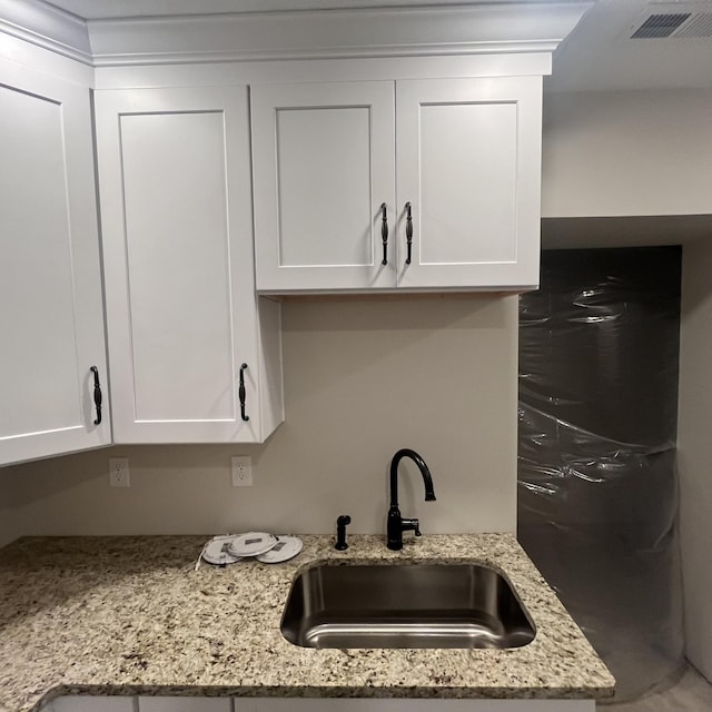 room details featuring light stone counters, sink, and white cabinetry