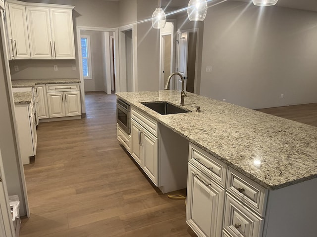 kitchen with light stone countertops, white cabinetry, a center island with sink, and sink