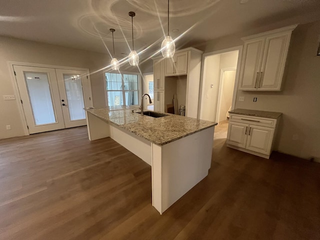 kitchen with a center island with sink, light stone countertops, white cabinets, and decorative light fixtures