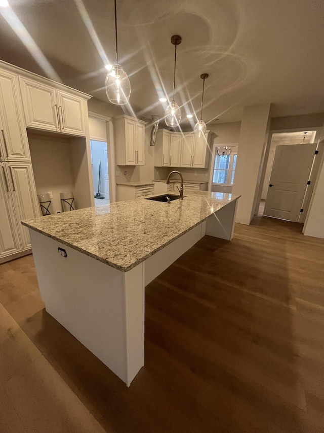 kitchen with sink, white cabinetry, pendant lighting, and light stone countertops