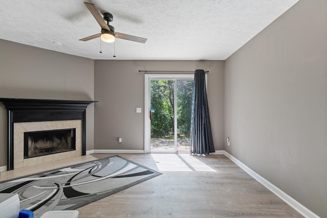 unfurnished living room featuring ceiling fan, a textured ceiling, a fireplace, and light hardwood / wood-style floors