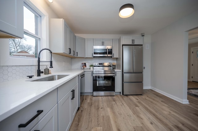 kitchen with sink, stainless steel appliances, tasteful backsplash, light stone counters, and light hardwood / wood-style floors