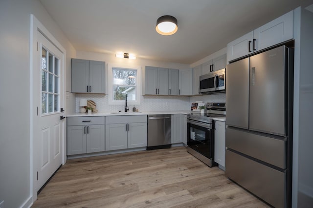 kitchen with sink, decorative backsplash, gray cabinets, appliances with stainless steel finishes, and light hardwood / wood-style floors