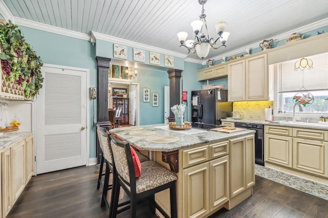 kitchen with light stone countertops, a center island, hanging light fixtures, cream cabinets, and black appliances