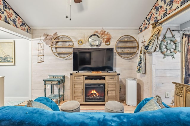 living room with ceiling fan, wood walls, crown molding, and a fireplace