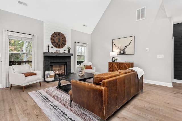 living room featuring light hardwood / wood-style floors, high vaulted ceiling, a healthy amount of sunlight, and a brick fireplace