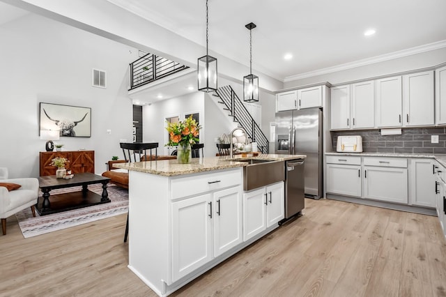 kitchen featuring a kitchen island with sink, sink, decorative light fixtures, light stone counters, and stainless steel appliances