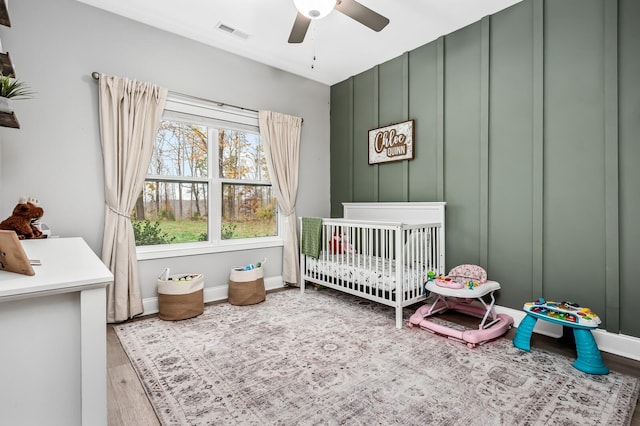 bedroom with ceiling fan, wood-type flooring, and a crib