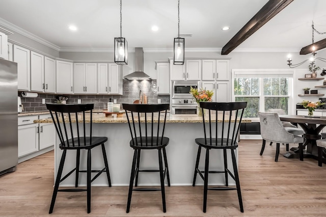 kitchen featuring appliances with stainless steel finishes, decorative light fixtures, a kitchen island with sink, and wall chimney range hood