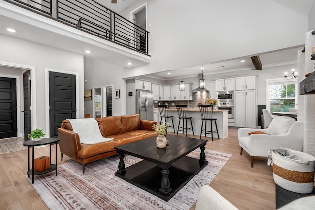 living room with beamed ceiling, light wood-type flooring, a towering ceiling, and an inviting chandelier