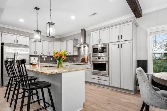 kitchen featuring wall chimney exhaust hood, tasteful backsplash, light stone counters, an island with sink, and appliances with stainless steel finishes