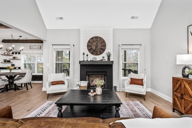 living room with a fireplace, an inviting chandelier, lofted ceiling, and light wood-type flooring