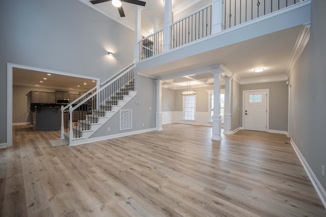 unfurnished living room featuring ceiling fan with notable chandelier, light wood-type flooring, ornamental molding, and a high ceiling