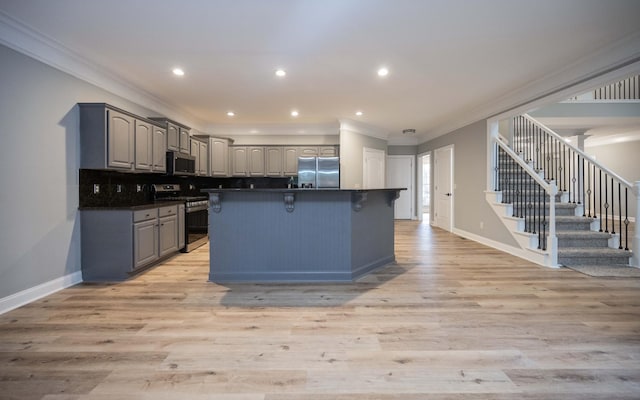 kitchen featuring appliances with stainless steel finishes, gray cabinetry, a kitchen island with sink, crown molding, and light hardwood / wood-style floors