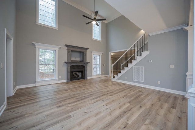 unfurnished living room with a towering ceiling, light hardwood / wood-style floors, ceiling fan, and crown molding