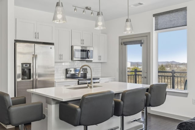 kitchen with a mountain view, backsplash, a kitchen island with sink, appliances with stainless steel finishes, and white cabinetry