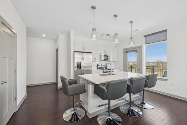 kitchen with white cabinetry, sink, stainless steel appliances, pendant lighting, and a center island with sink