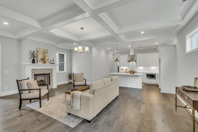 living room with dark wood-type flooring, coffered ceiling, a stone fireplace, beamed ceiling, and a chandelier