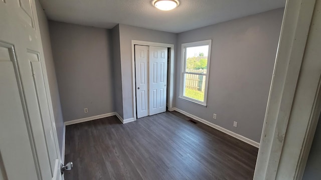 unfurnished bedroom featuring a textured ceiling, dark wood-type flooring, and a closet