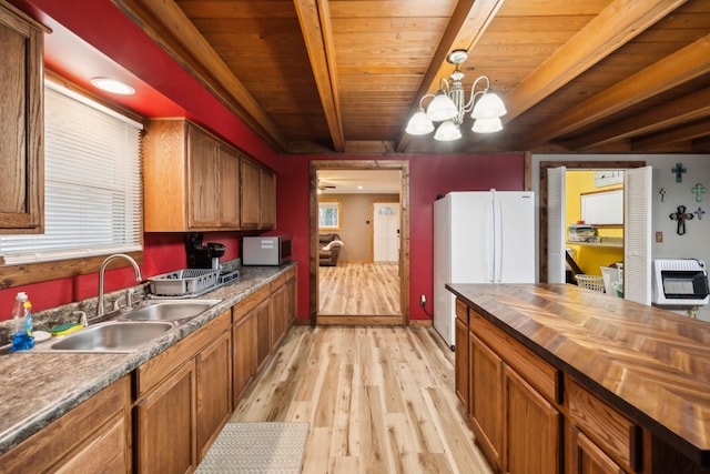 kitchen featuring sink, hanging light fixtures, beamed ceiling, a notable chandelier, and white fridge