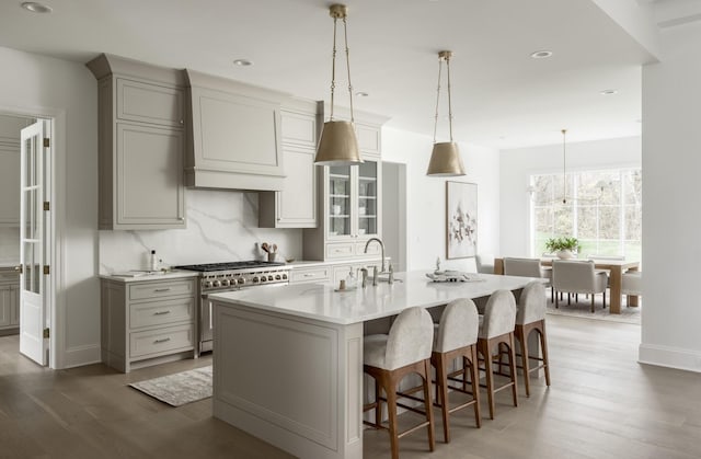 kitchen featuring tasteful backsplash, an island with sink, pendant lighting, a breakfast bar area, and stainless steel stove