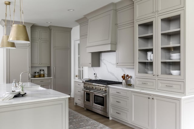 kitchen featuring double oven range, dark wood-type flooring, sink, decorative light fixtures, and light stone counters