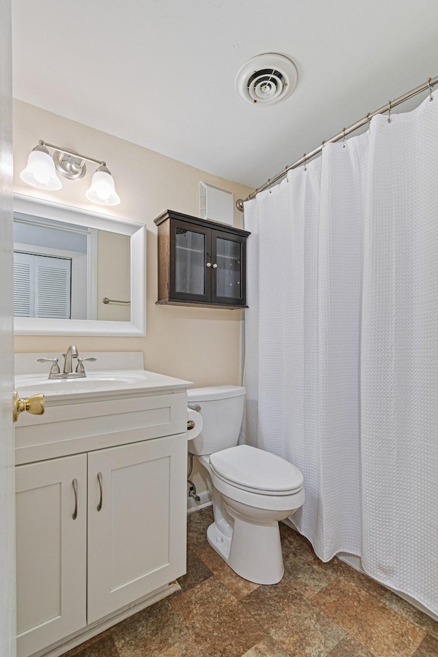 bathroom featuring vanity, a shower with curtain, visible vents, stone finish flooring, and toilet