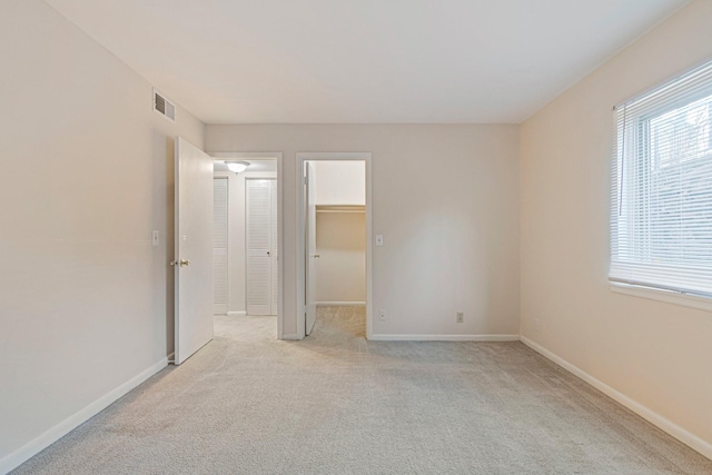 unfurnished bedroom featuring a walk in closet, multiple windows, visible vents, and light carpet