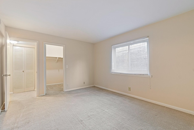 unfurnished bedroom featuring baseboards, light carpet, a closet, and a walk in closet