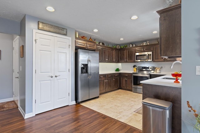 kitchen with dark brown cabinets, stainless steel appliances, light hardwood / wood-style flooring, and sink