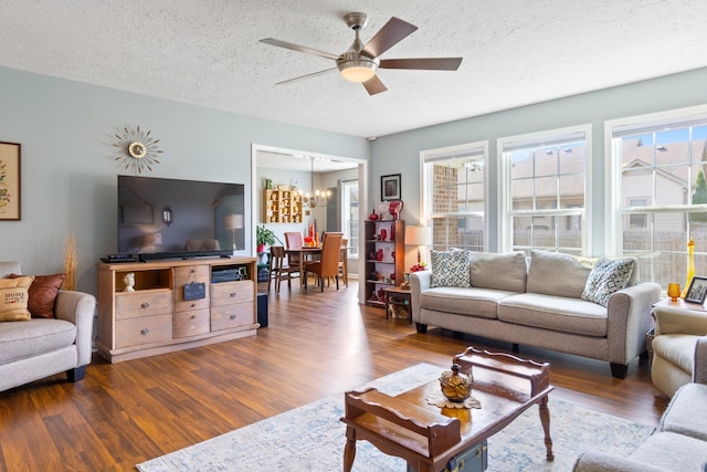 living room featuring a textured ceiling, ceiling fan with notable chandelier, and dark wood-type flooring