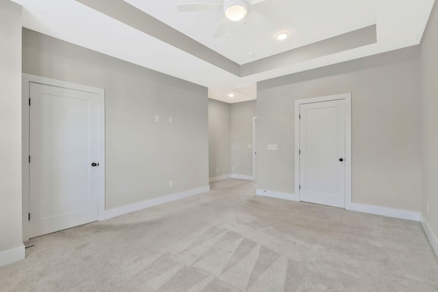 carpeted empty room featuring ceiling fan and a raised ceiling