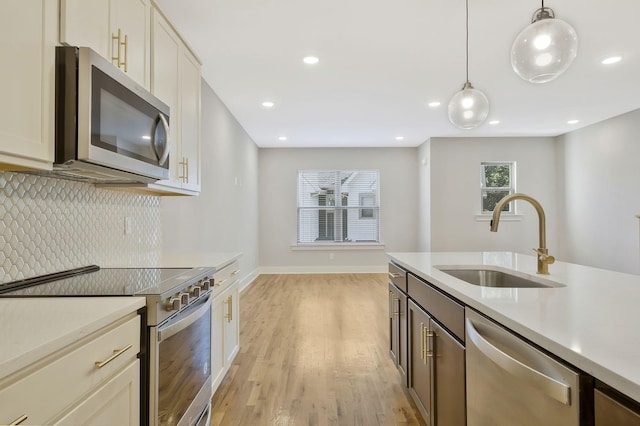 kitchen with decorative light fixtures, sink, decorative backsplash, stainless steel appliances, and light hardwood / wood-style flooring