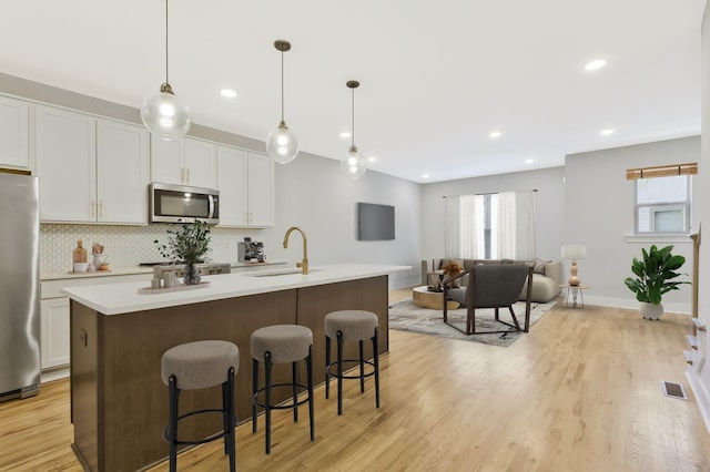 kitchen featuring sink, decorative light fixtures, stainless steel appliances, and an island with sink