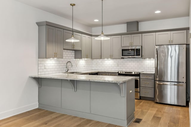 kitchen featuring sink, hanging light fixtures, stainless steel appliances, light stone counters, and kitchen peninsula