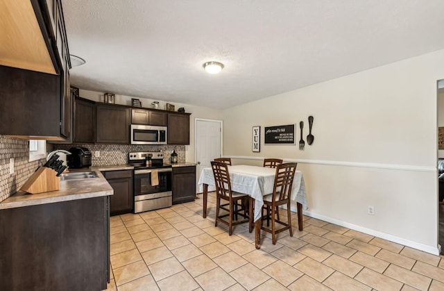 kitchen featuring decorative backsplash, dark brown cabinetry, stainless steel appliances, sink, and light tile patterned floors