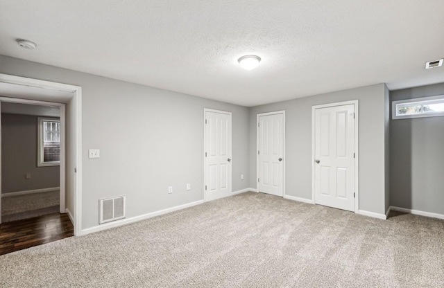 unfurnished bedroom featuring carpet flooring, a textured ceiling, and multiple closets