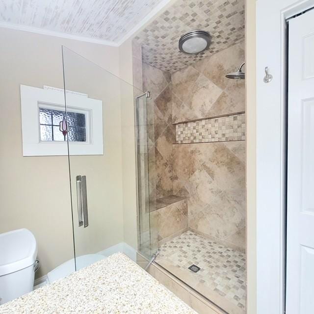 bathroom featuring crown molding, a shower with door, and toilet