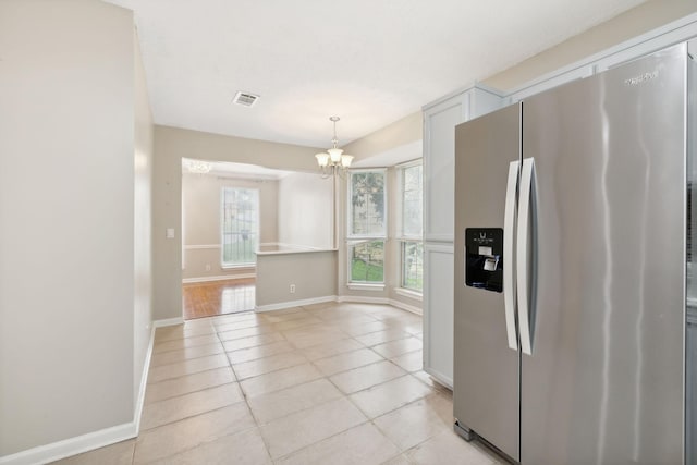 kitchen with light tile patterned floors, stainless steel fridge, pendant lighting, a chandelier, and white cabinets