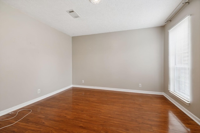 empty room with a textured ceiling, plenty of natural light, and dark wood-type flooring